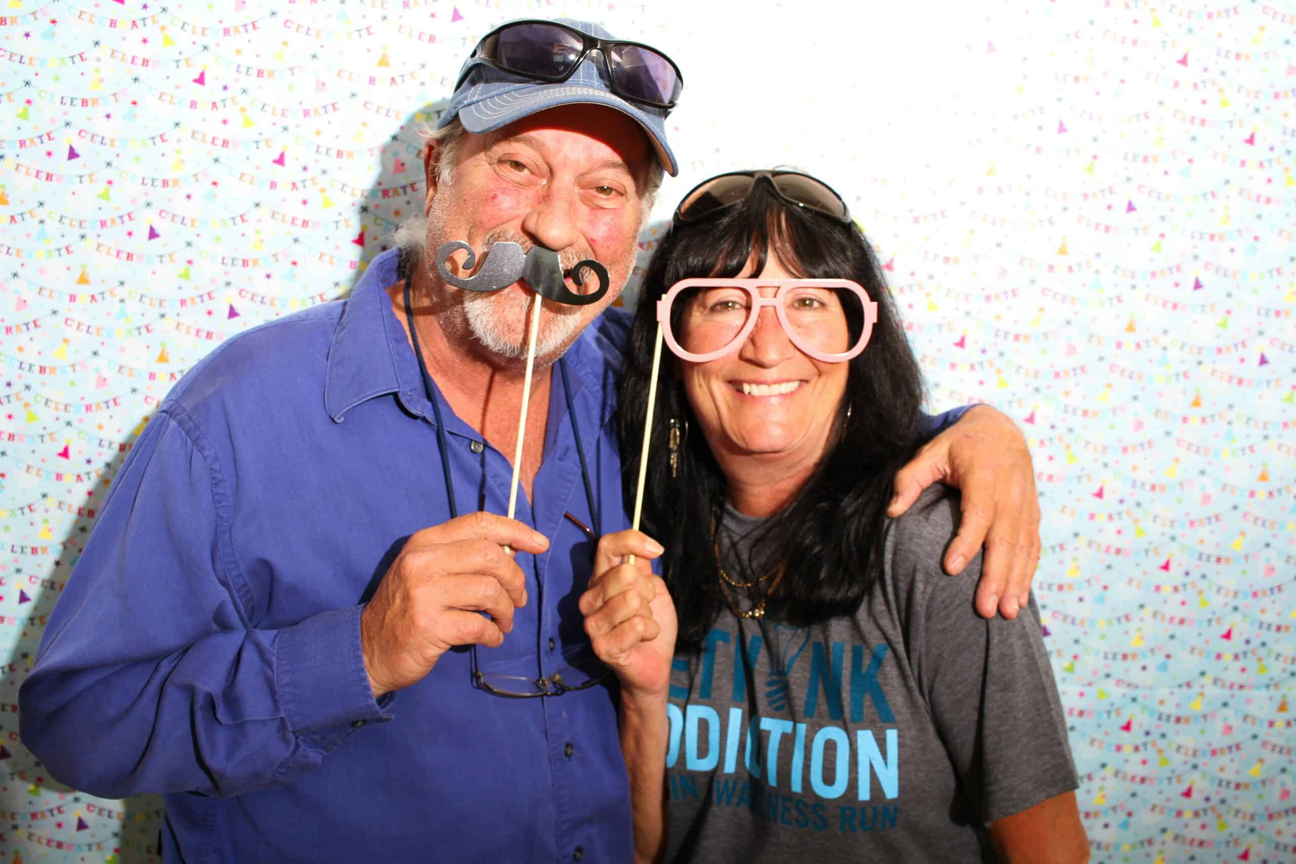 Couple holding mustache and glasses props together at confetti backdrop