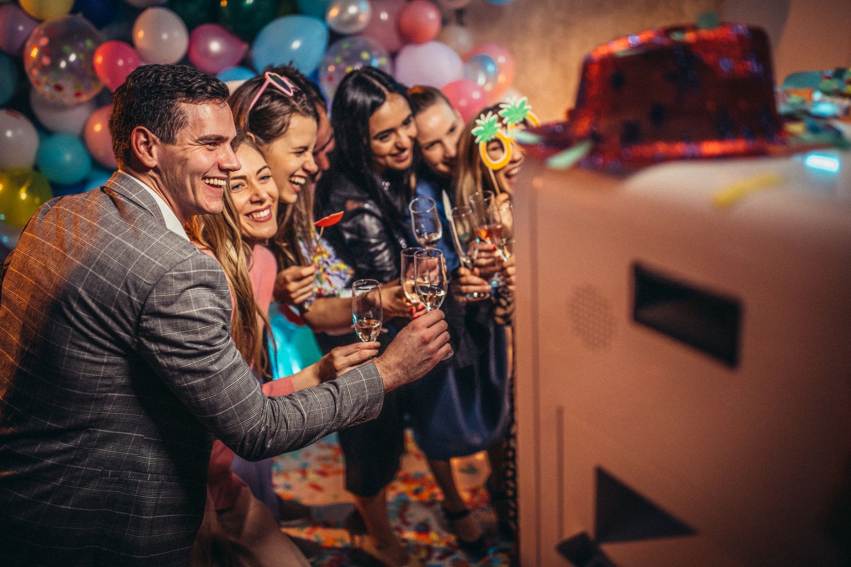 Group of friends celebrating with champagne next to photo booth at party