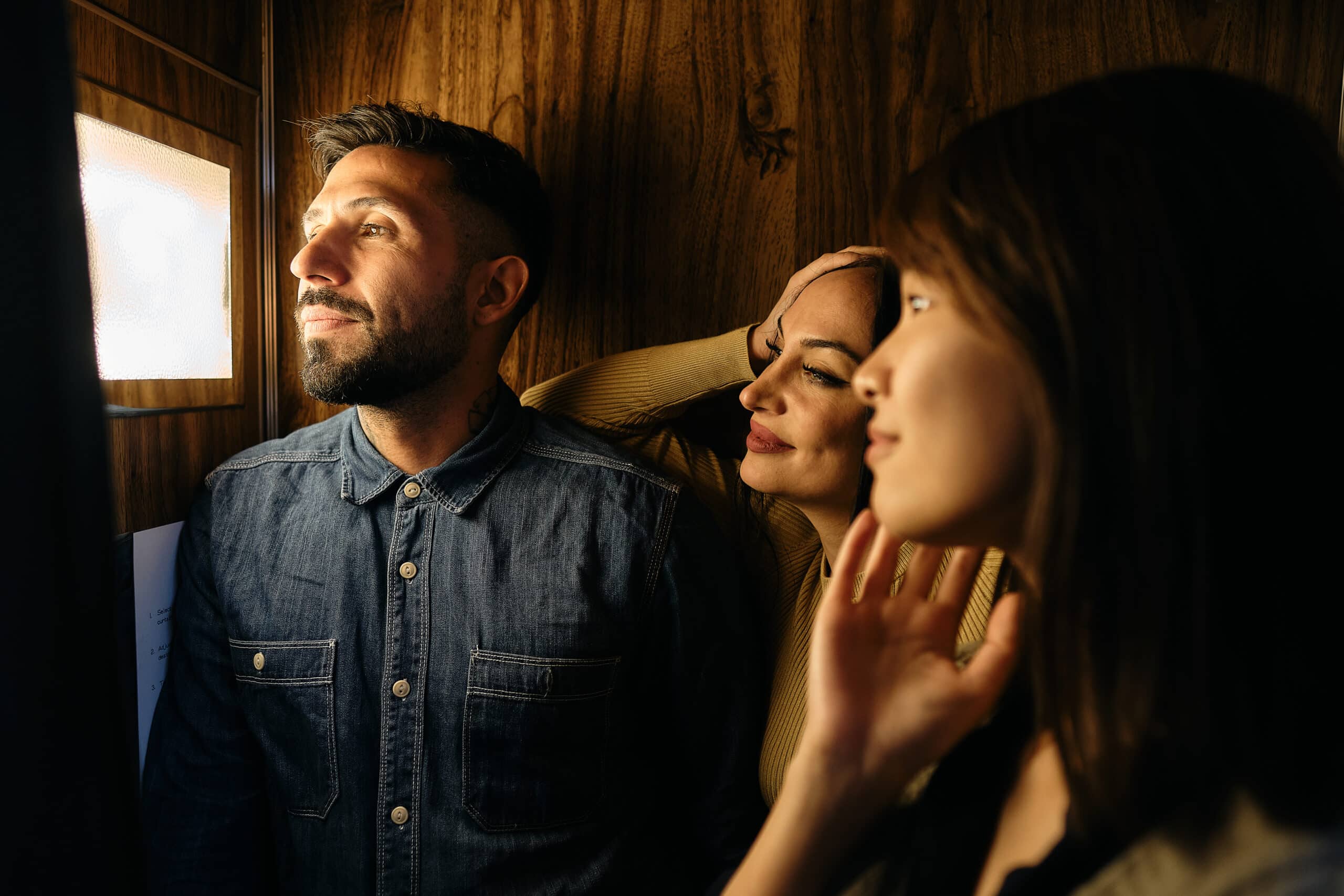 Three friends posing thoughtfully inside warm wood-paneled photo booth