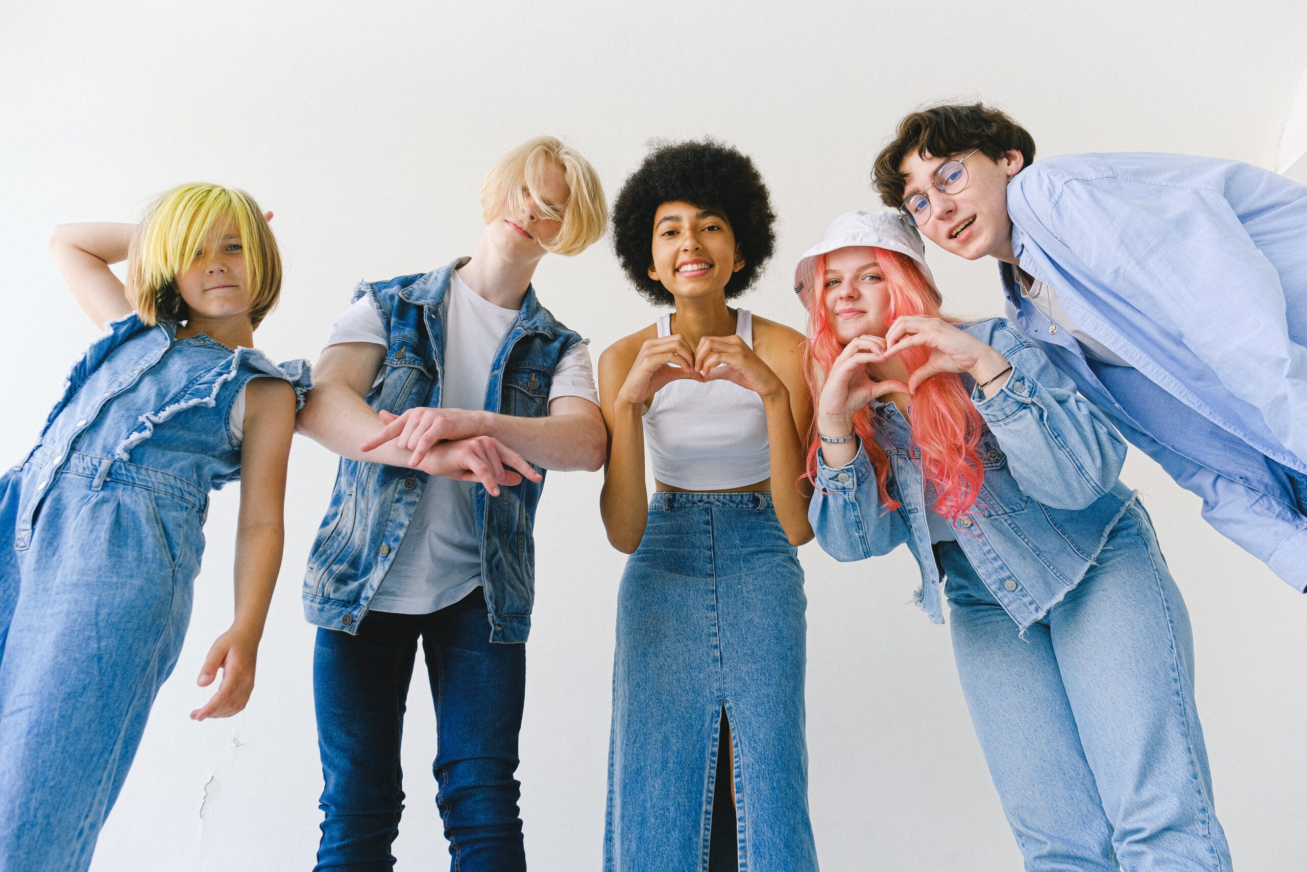 Four young people in coordinated denim outfits posing playfully at studio