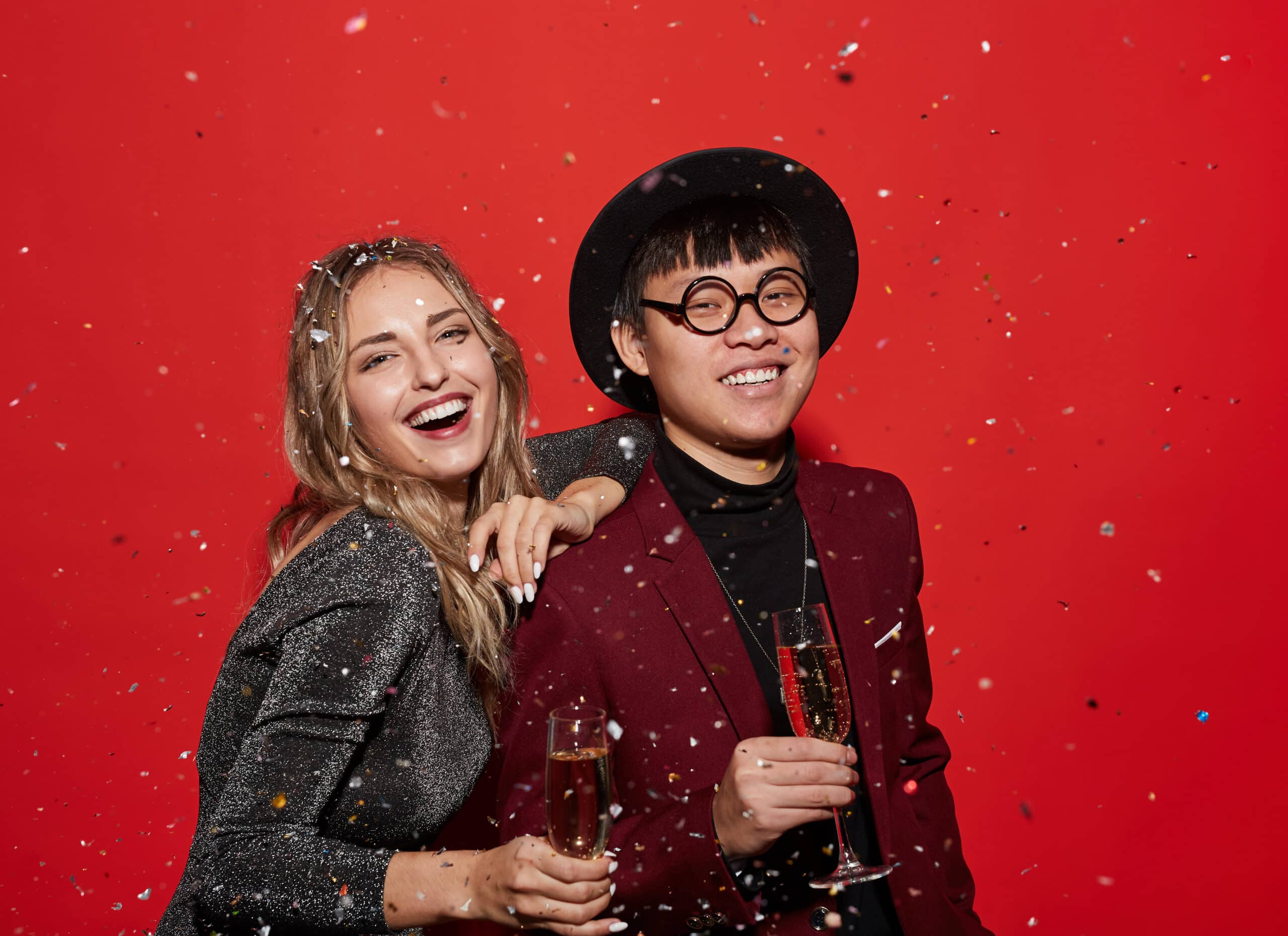Couple celebrating with champagne in front of red confetti backdrop