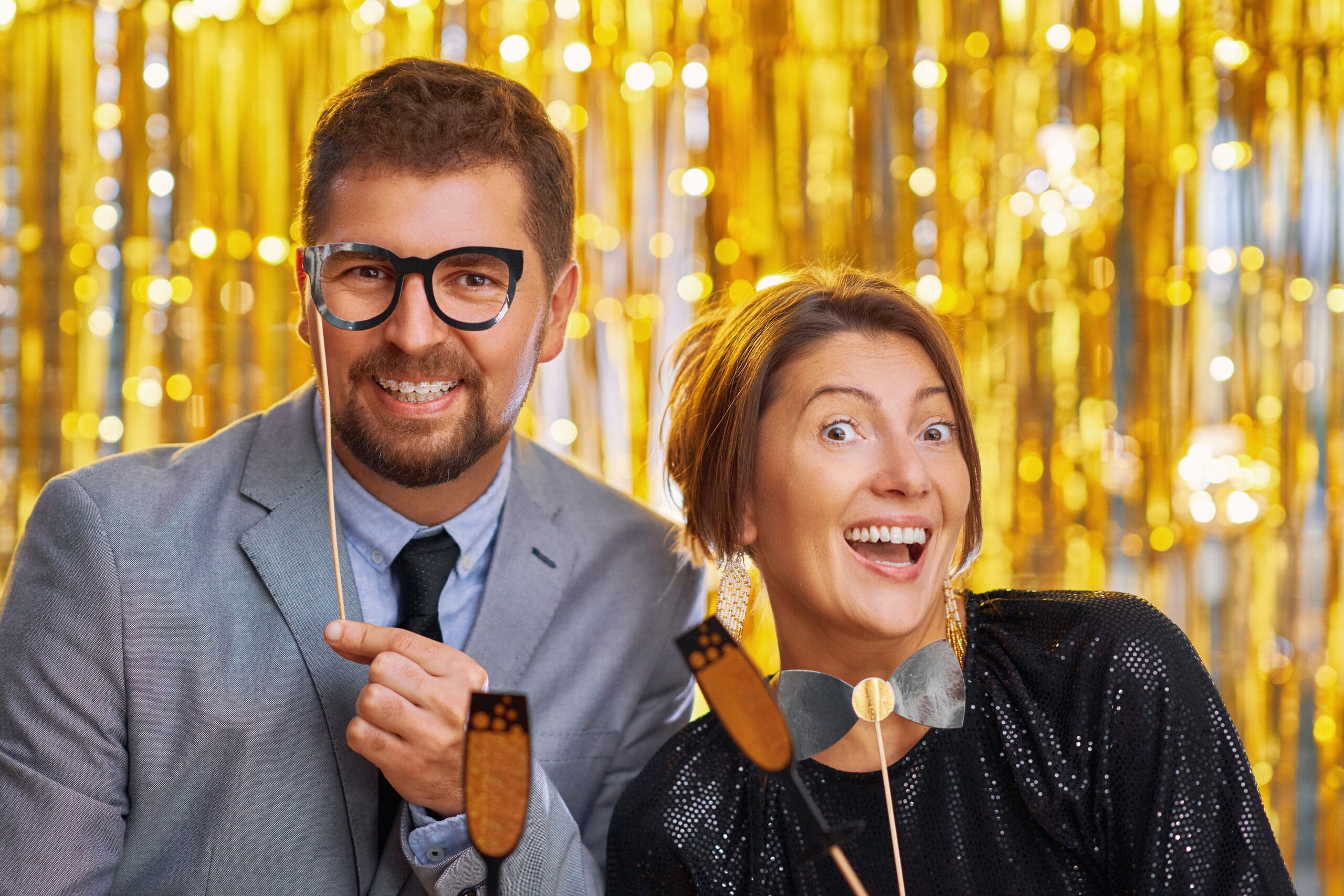 Couple holding props at gold metallic curtain photo booth backdrop