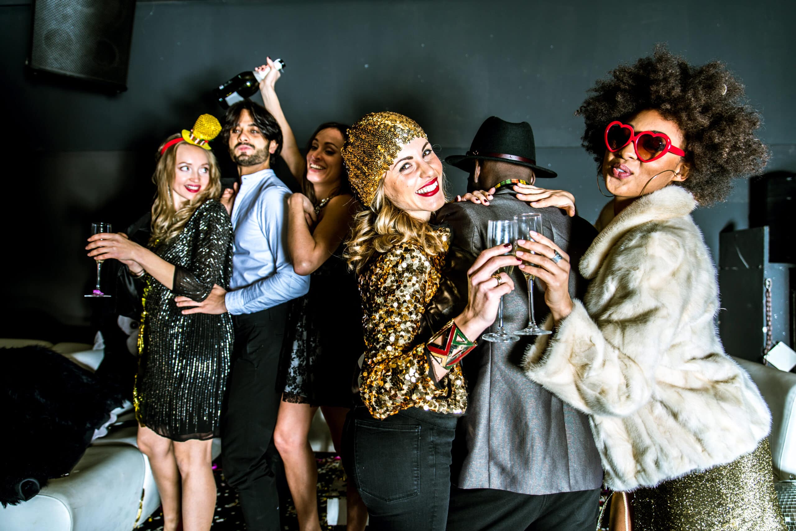 Group of friends in party attire celebrating with champagne and gold prop