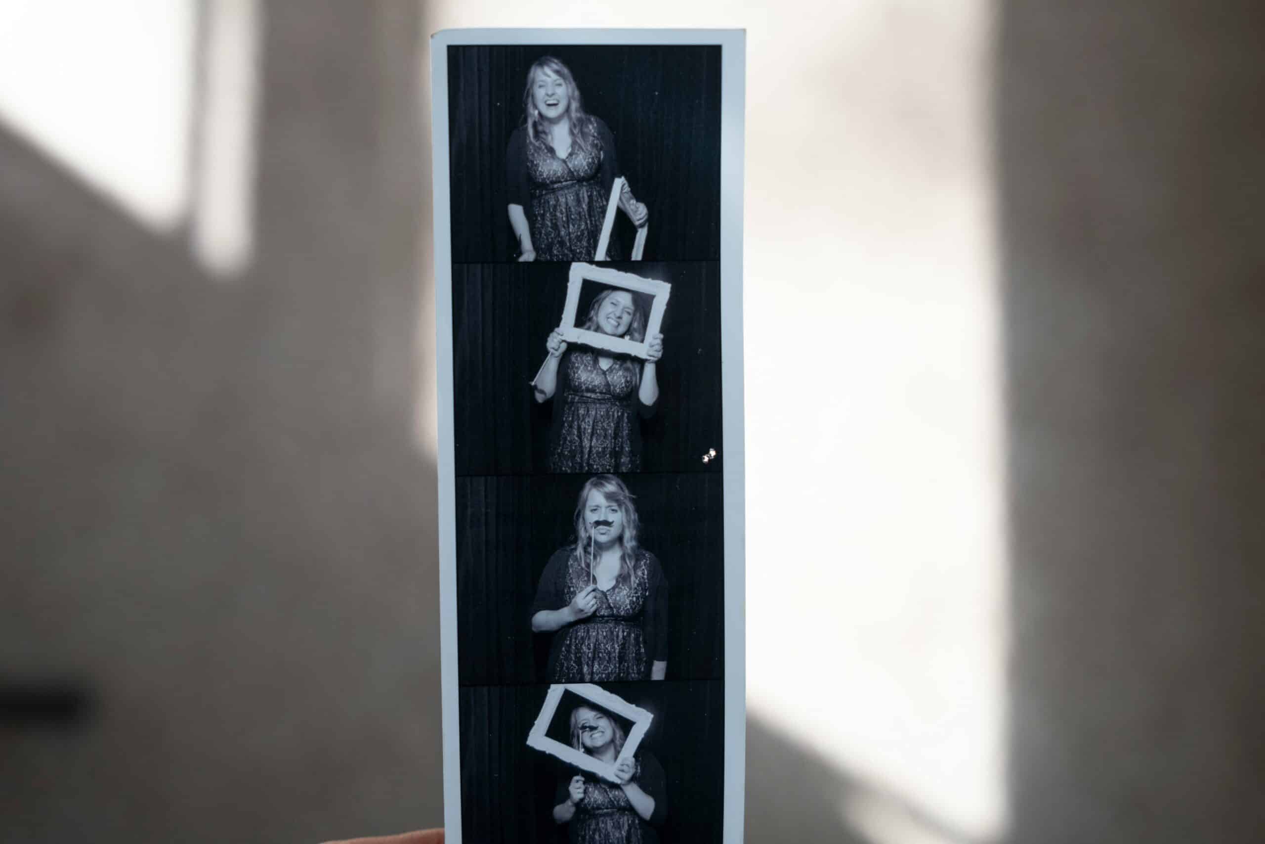 Vertical photo booth strip showing person holding framed photos in monochrome