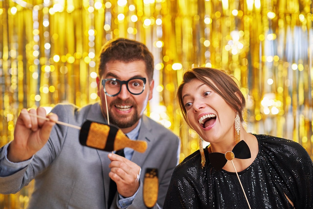 Couple holding mustache and earring props at gold metallic curtain backdrop