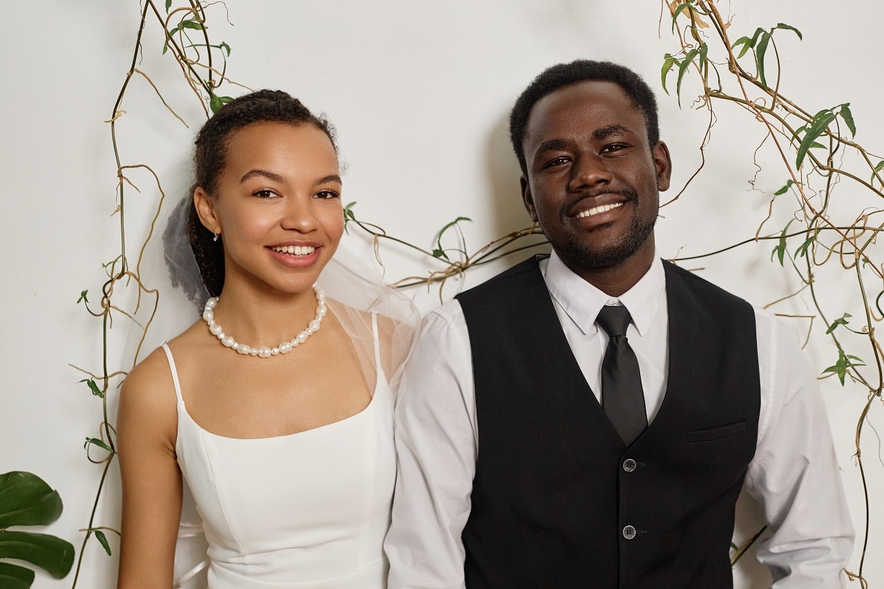 Elegant bride and groom smiling together at greenery-draped wedding backdrop