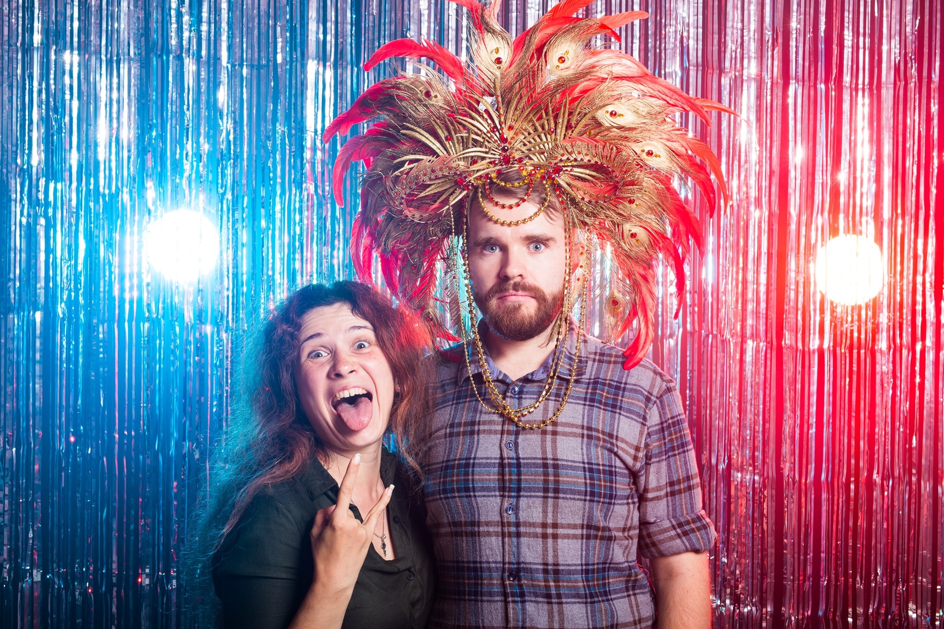 Couple wearing oversized red feather headdress at colorful tinsel backdrop