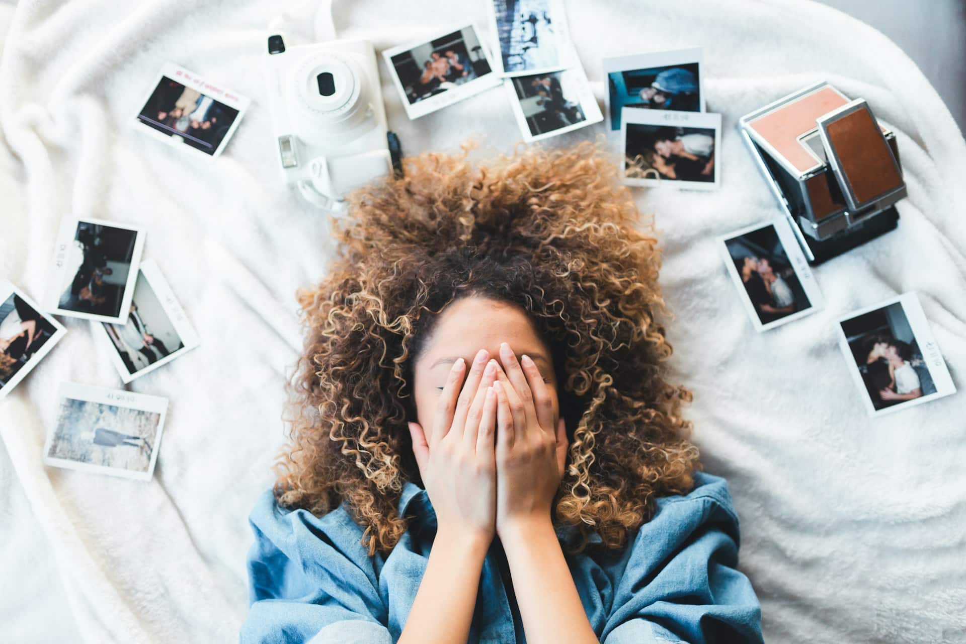 Woman lying with curly hair surrounded by scattered Polaroid photos