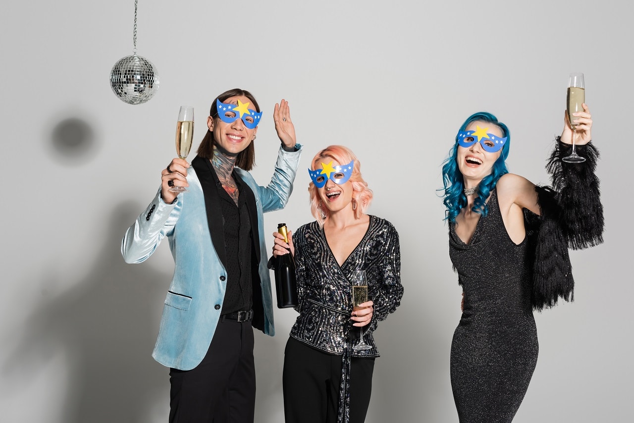 Three women in mardi gras style masks celebrating with champagne and disco ball