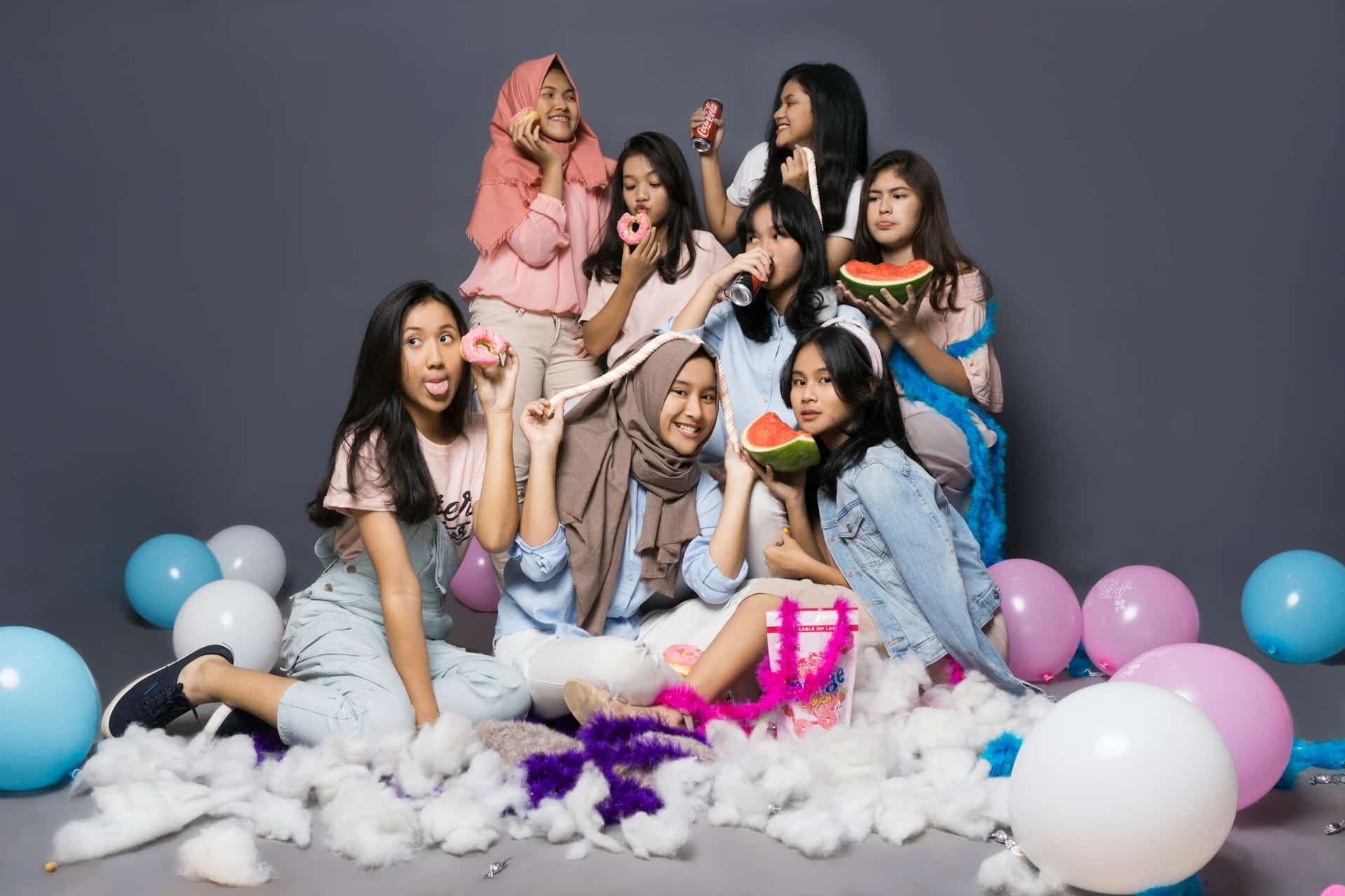 Group of friends in casual outfits posing playfully with balloons at studio backdrop
