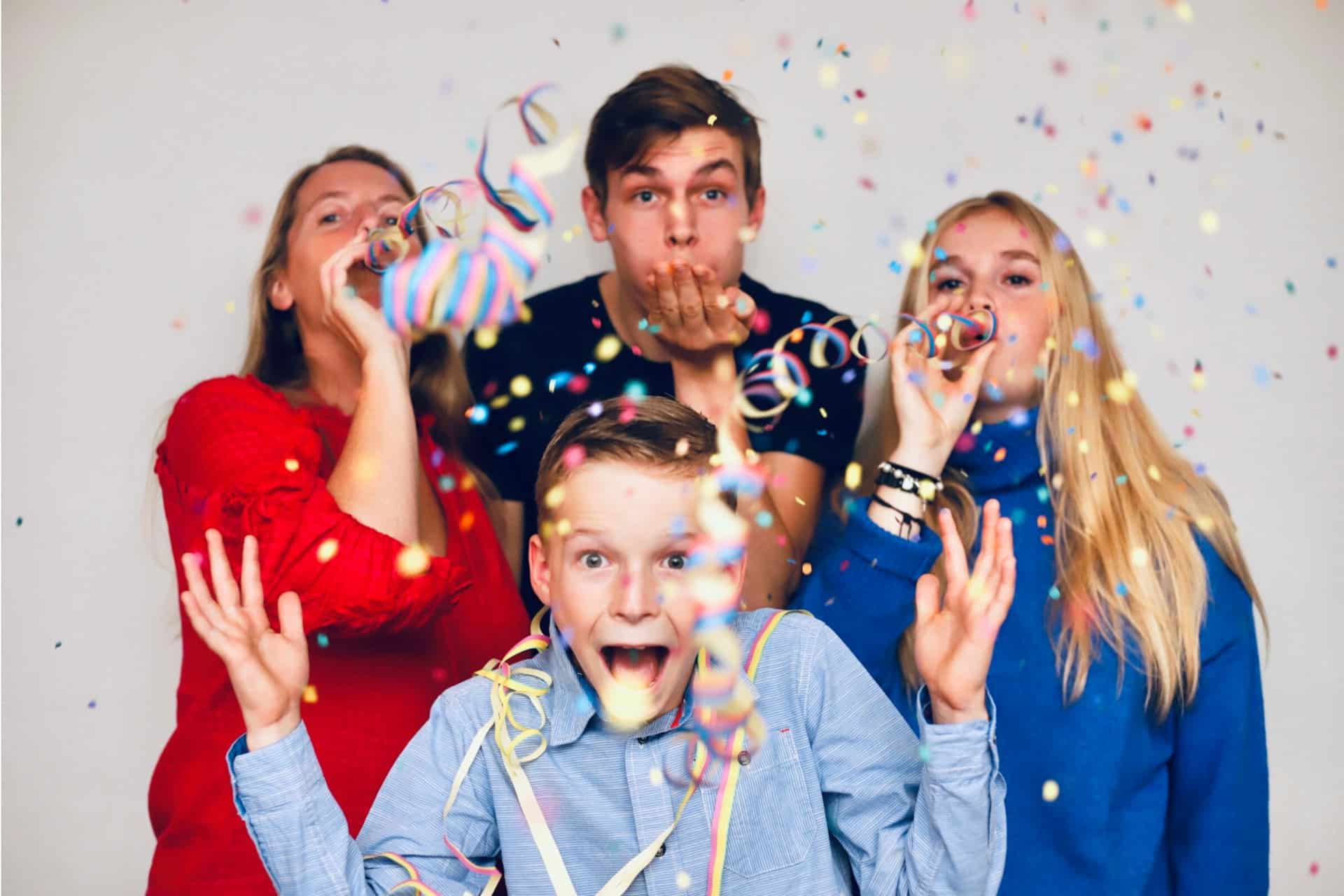 Family of four celebrating with confetti and party props at white backdrop