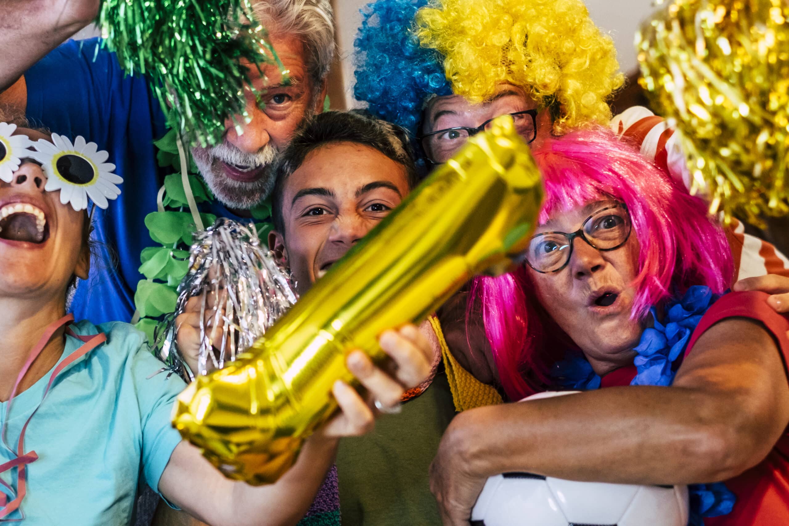 Family of mixed ages celebrating with colorful wigs and inflatable props