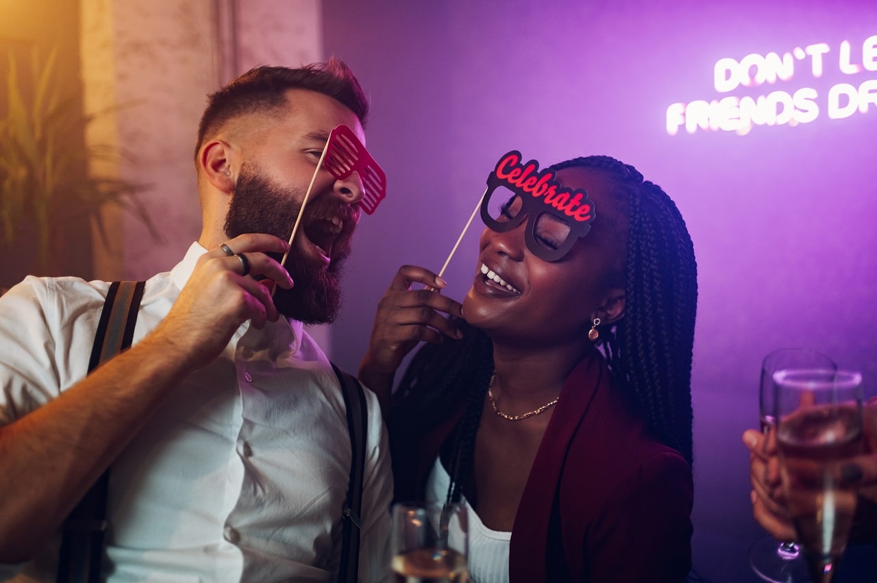 Couple holding lip and mustache props with neon sign at club party