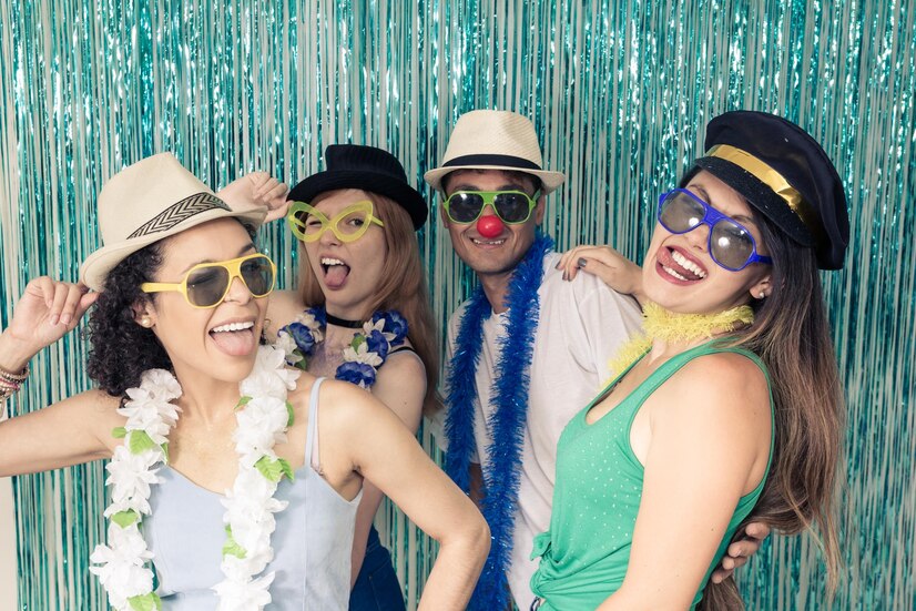 Group of friends in fedora hats and leis posing playfully at teal tinsel backdrop