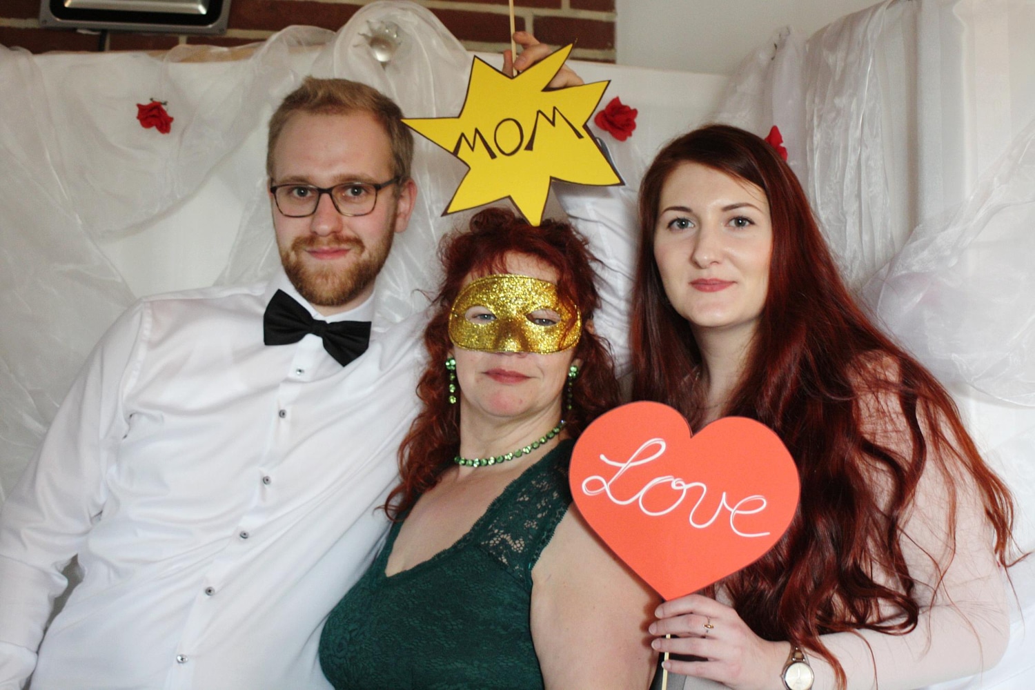 Couple in formal attire with masquerade mask and Mom and Love props at angel backdrop