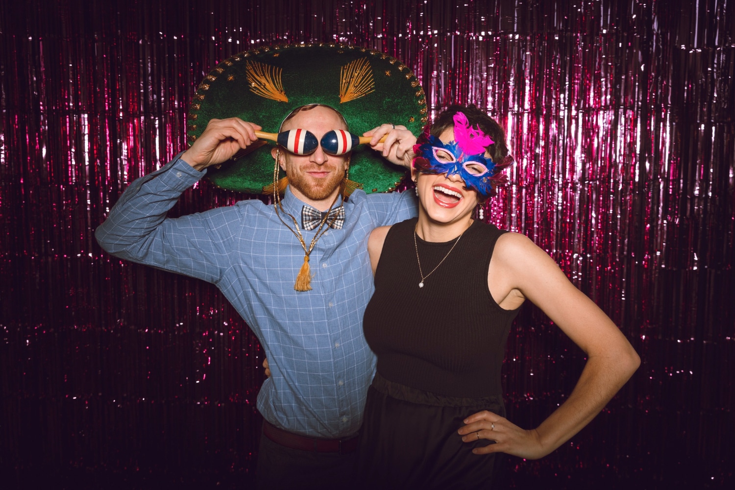 Couple in carnival masks and oversized glasses at pink tinsel backdrop