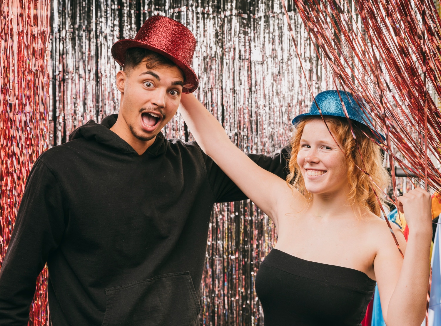 Couple wearing red and blue fedora props at red tinsel curtain backdrop