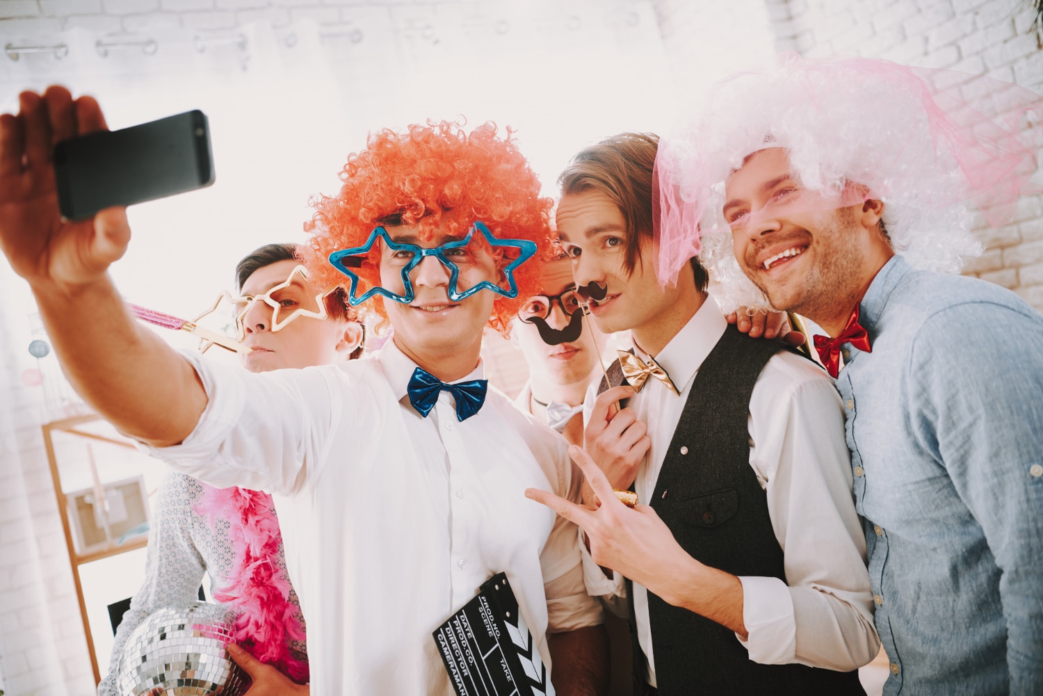 Group of friends in colorful wigs taking selfie at lively photo booth party