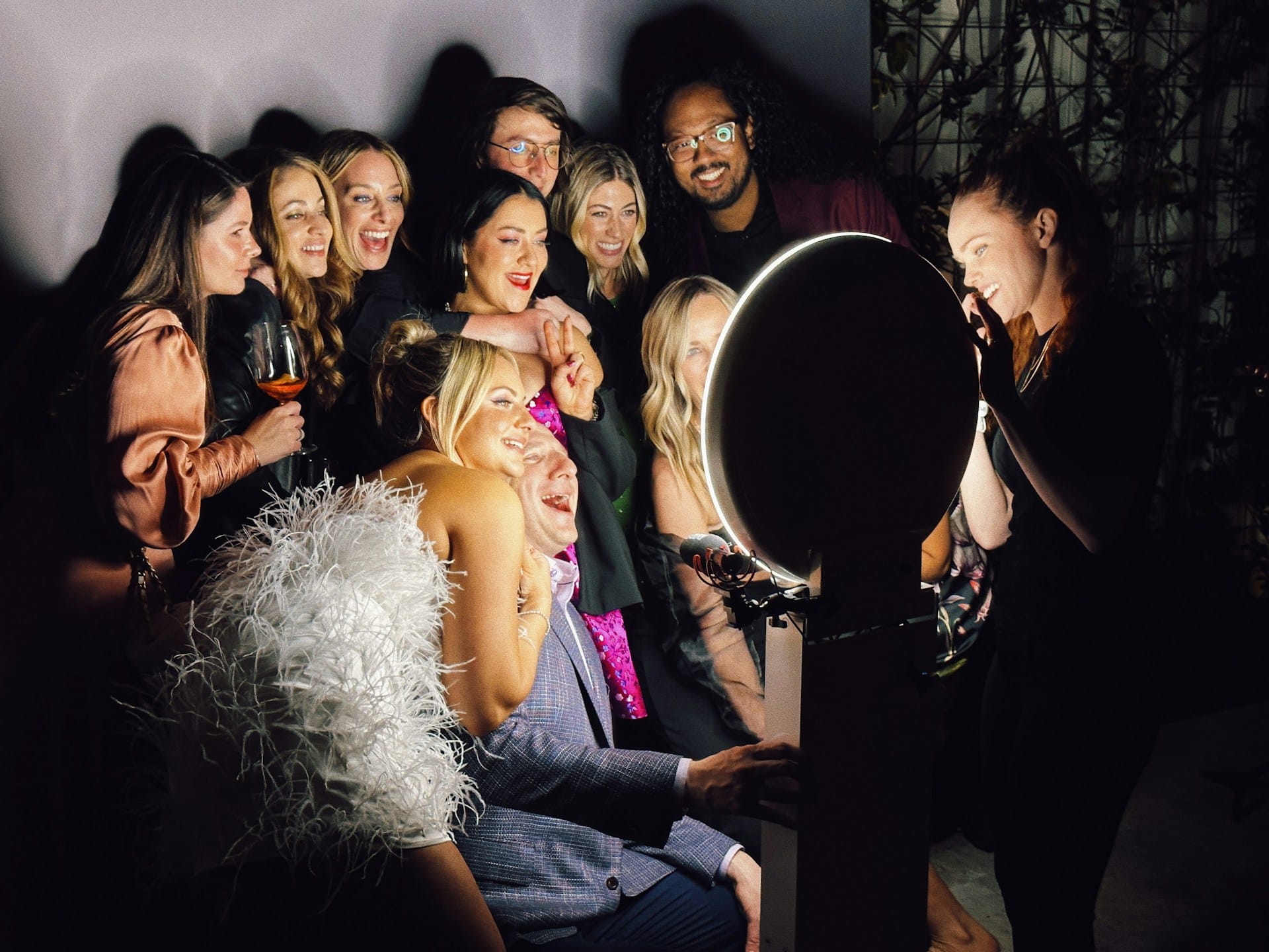 Group of friends gathered around photo booth ring light at evening party