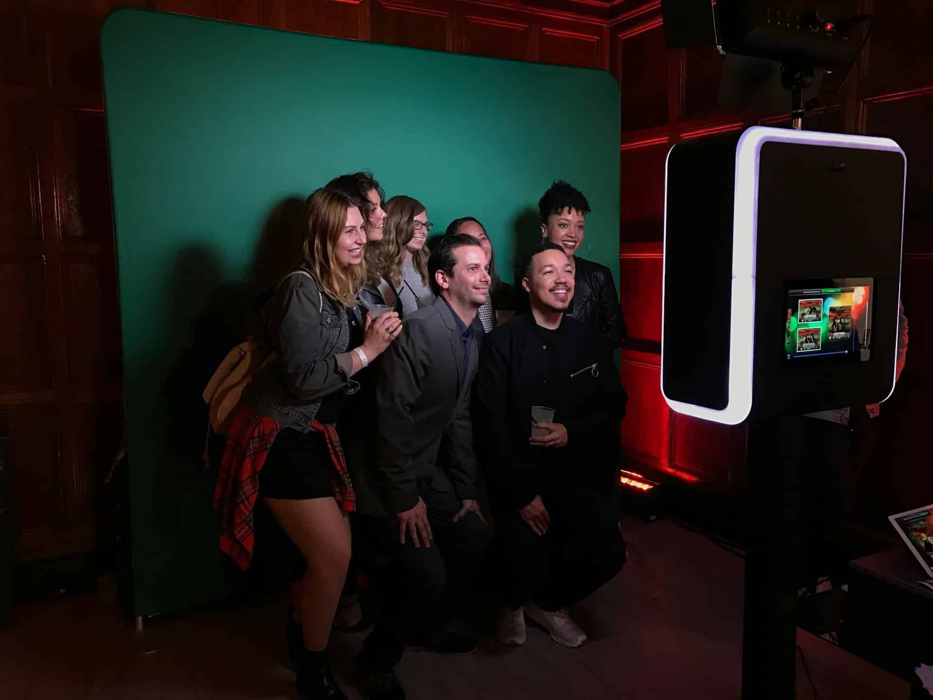 Group posing in front of green screen photo booth with monitor display