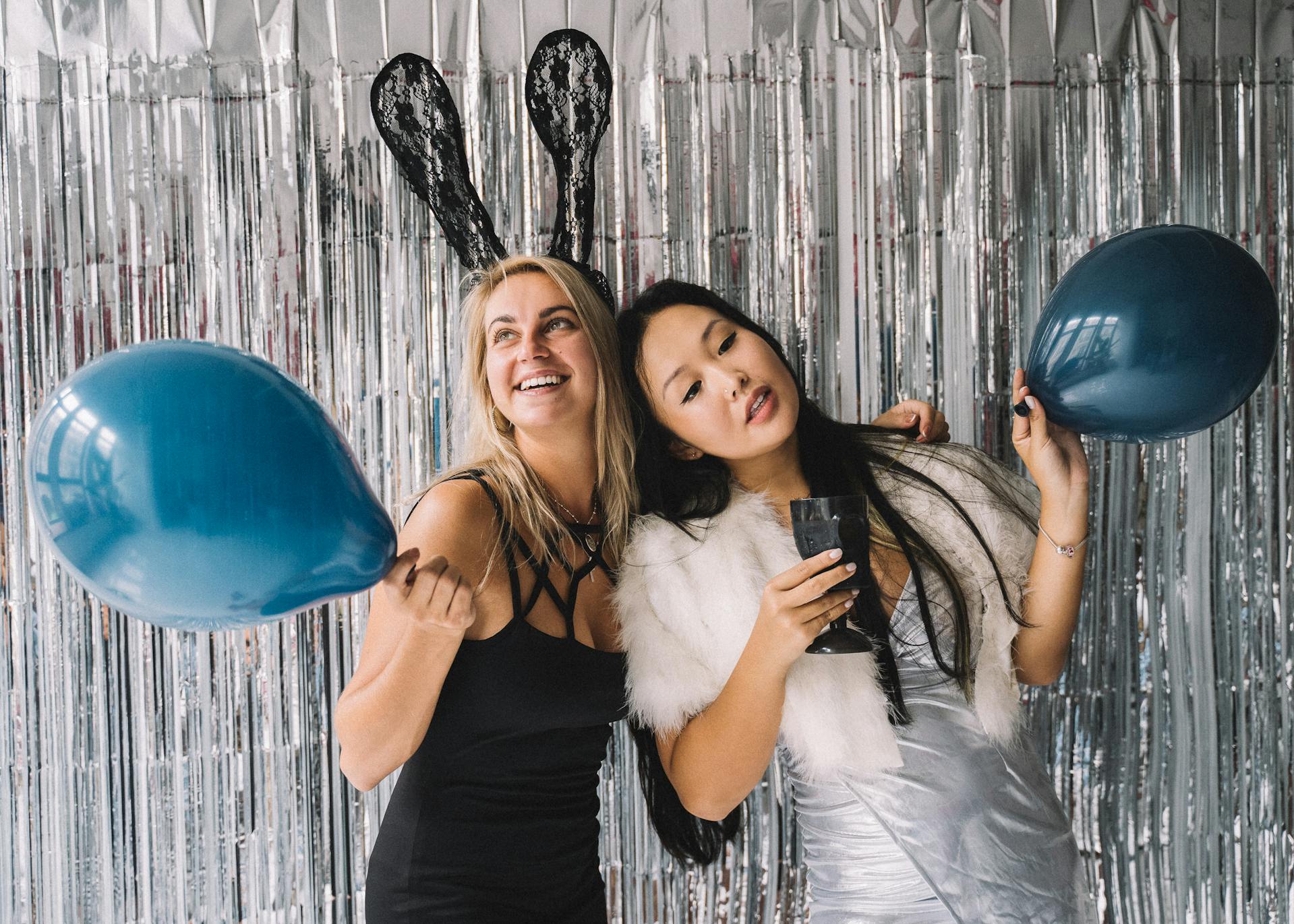 Two women holding blue balloons with bunny ears at silver tinsel backdrop