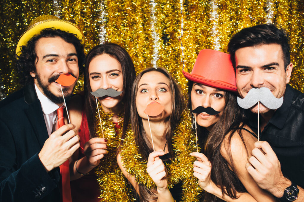 Group of friends holding mustache and lip props at gold tinsel photo booth backdrop