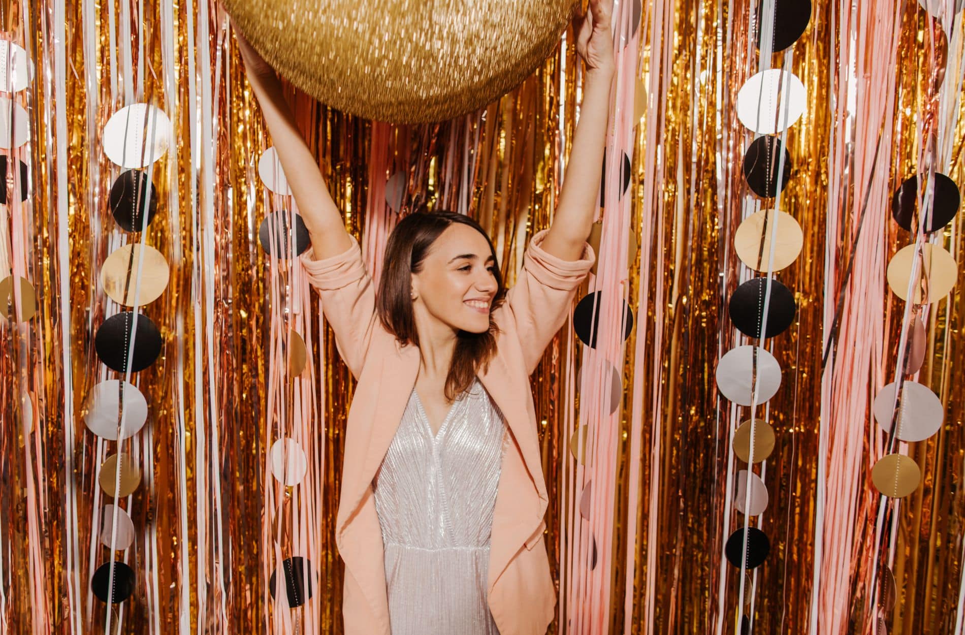 Woman in sequin top holding gold balloon at gold confetti backdrop