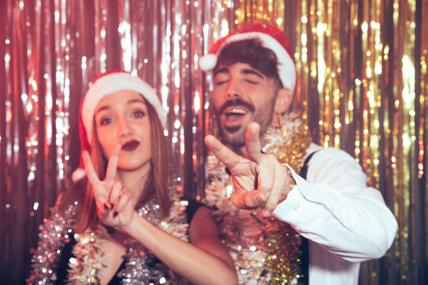 Couple in Santa hats and tinsel boas posing at gold sequin photo booth backdrop