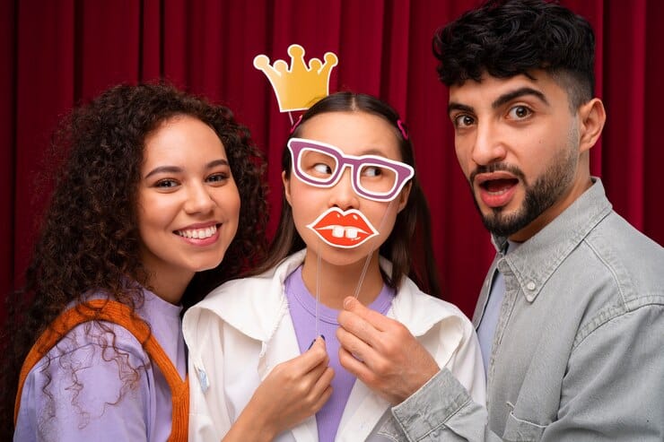 Three friends with crown and oversized glasses props at red curtain backdrop