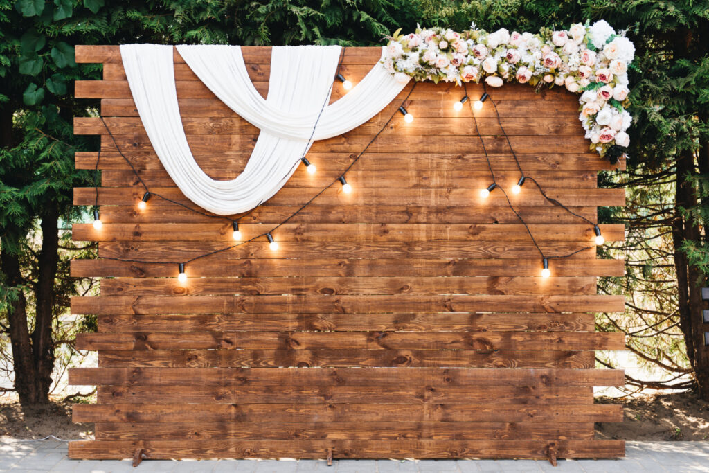 Rustic wooden plank backdrop with white draping, string lights and floral garland