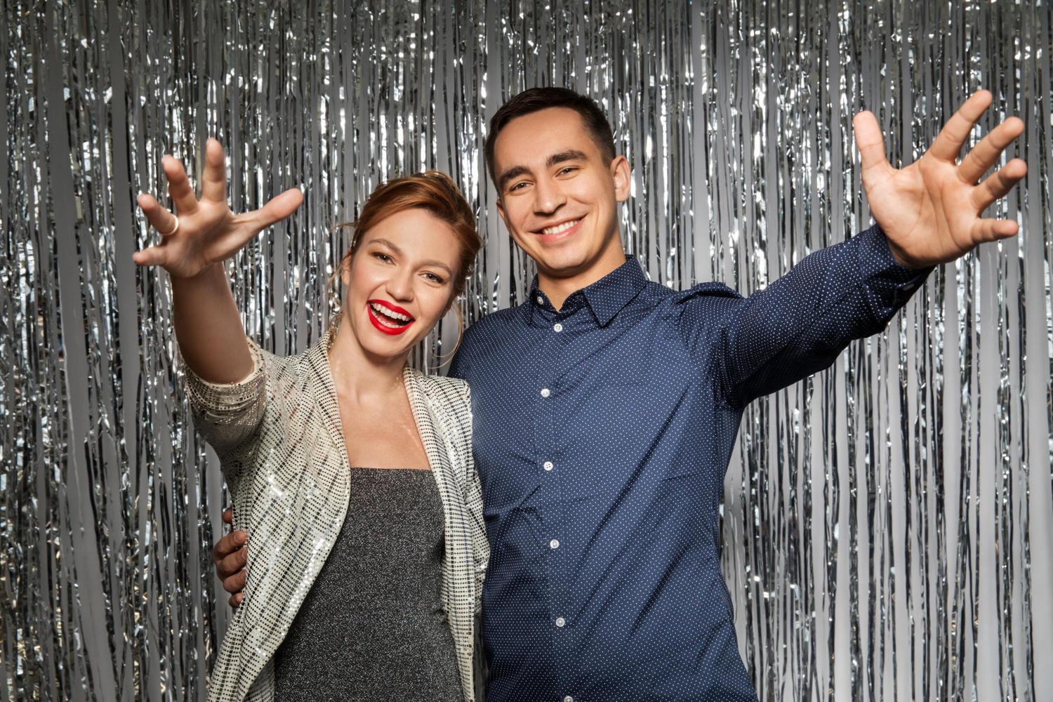 Couple stretching arms playfully at silver tinsel curtain photo booth backdrop